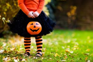 a little girl dressed up as a witch while holding a jack-o-lantern