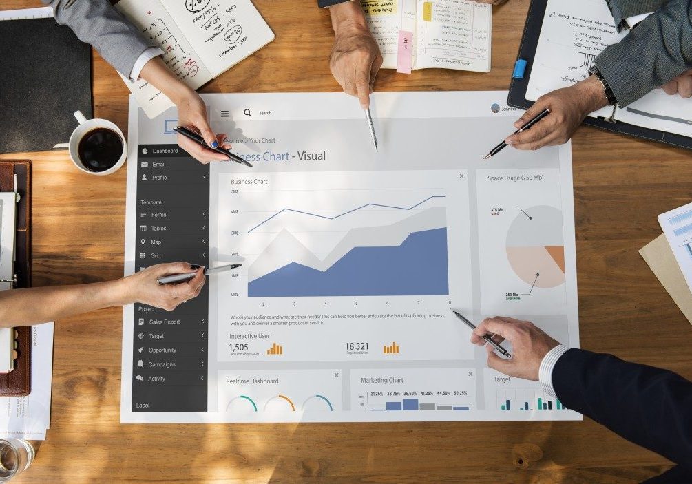 group of people having a meeting while holding a pen pointing to a visual chart group of people having a meeting while holding a pen pointing to a visual chart